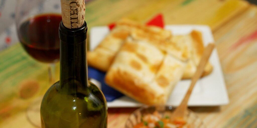 botella de vino tinto sobre mesa con copa servida y empanadas comida típica chilena