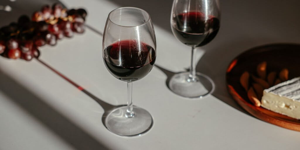 copas de vino tinto en una mesa blanca con comida y uvas